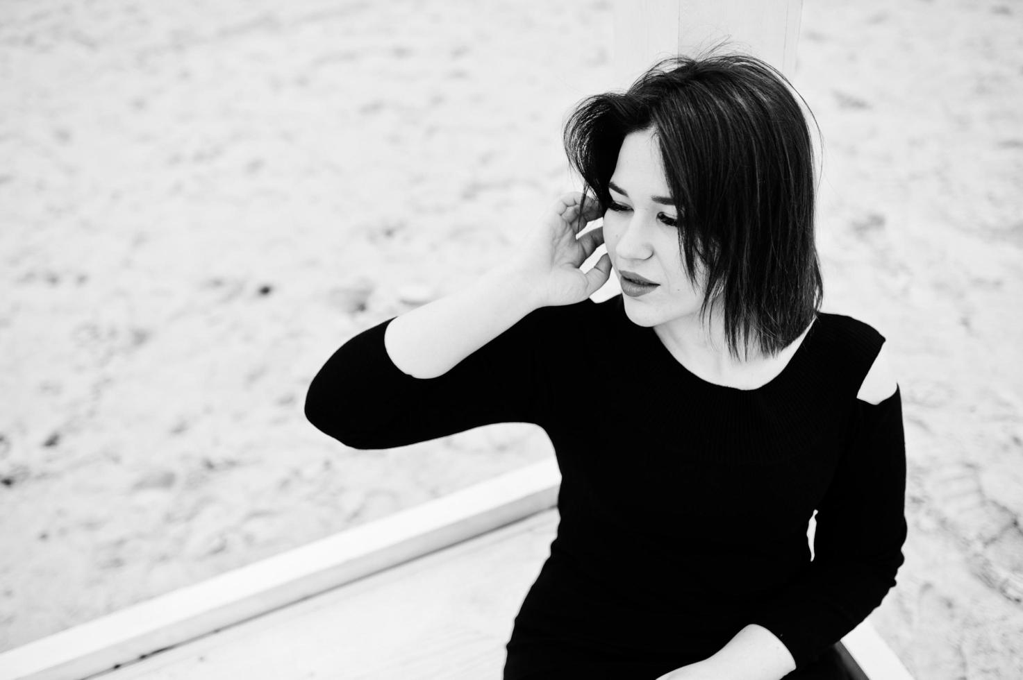 portrait de jeune fille brune en robe noire assis à la construction en bois blanc. photo