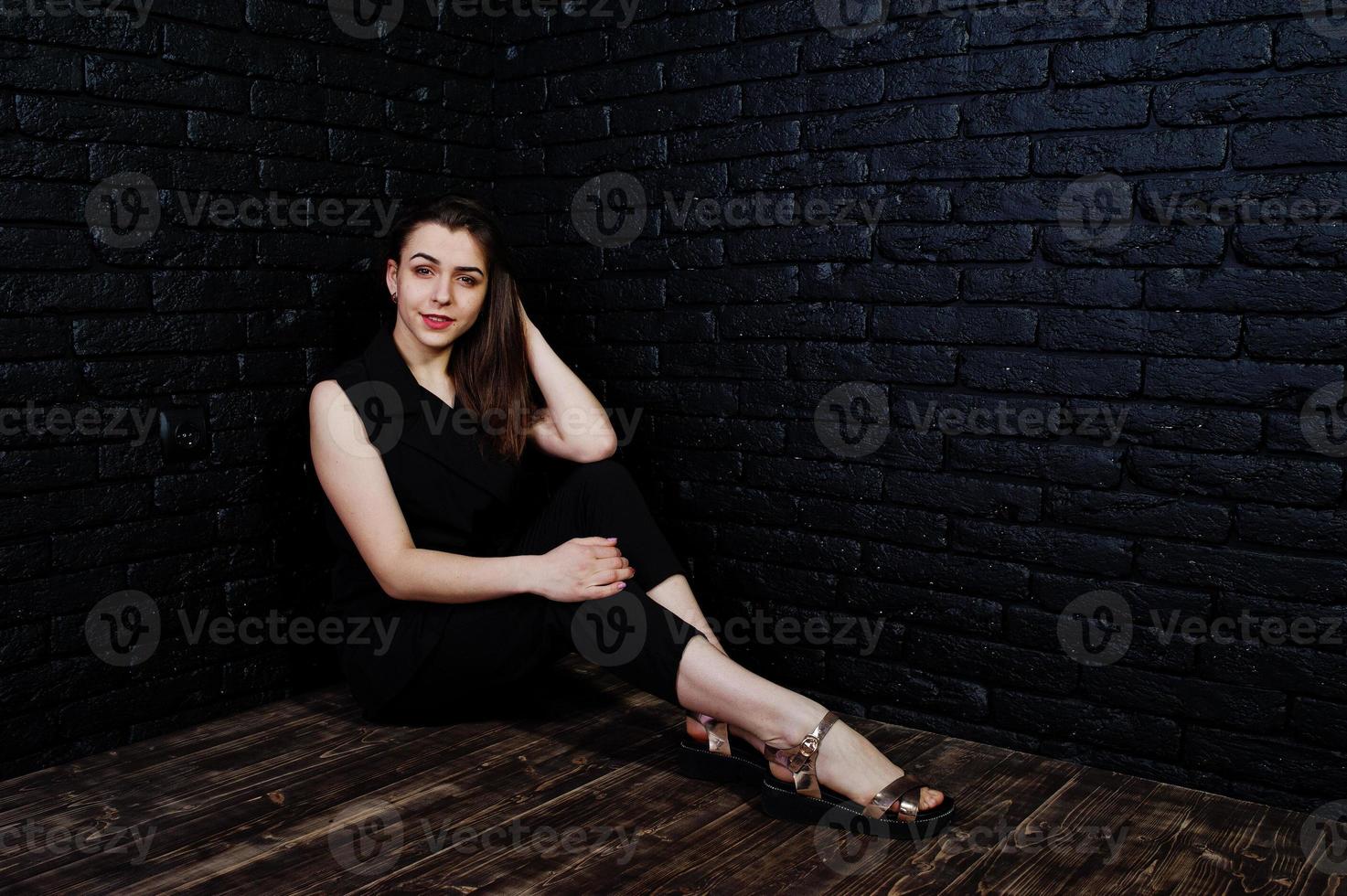 portrait d'une belle fille brune en combinaison noire assise et posant en studio. photo