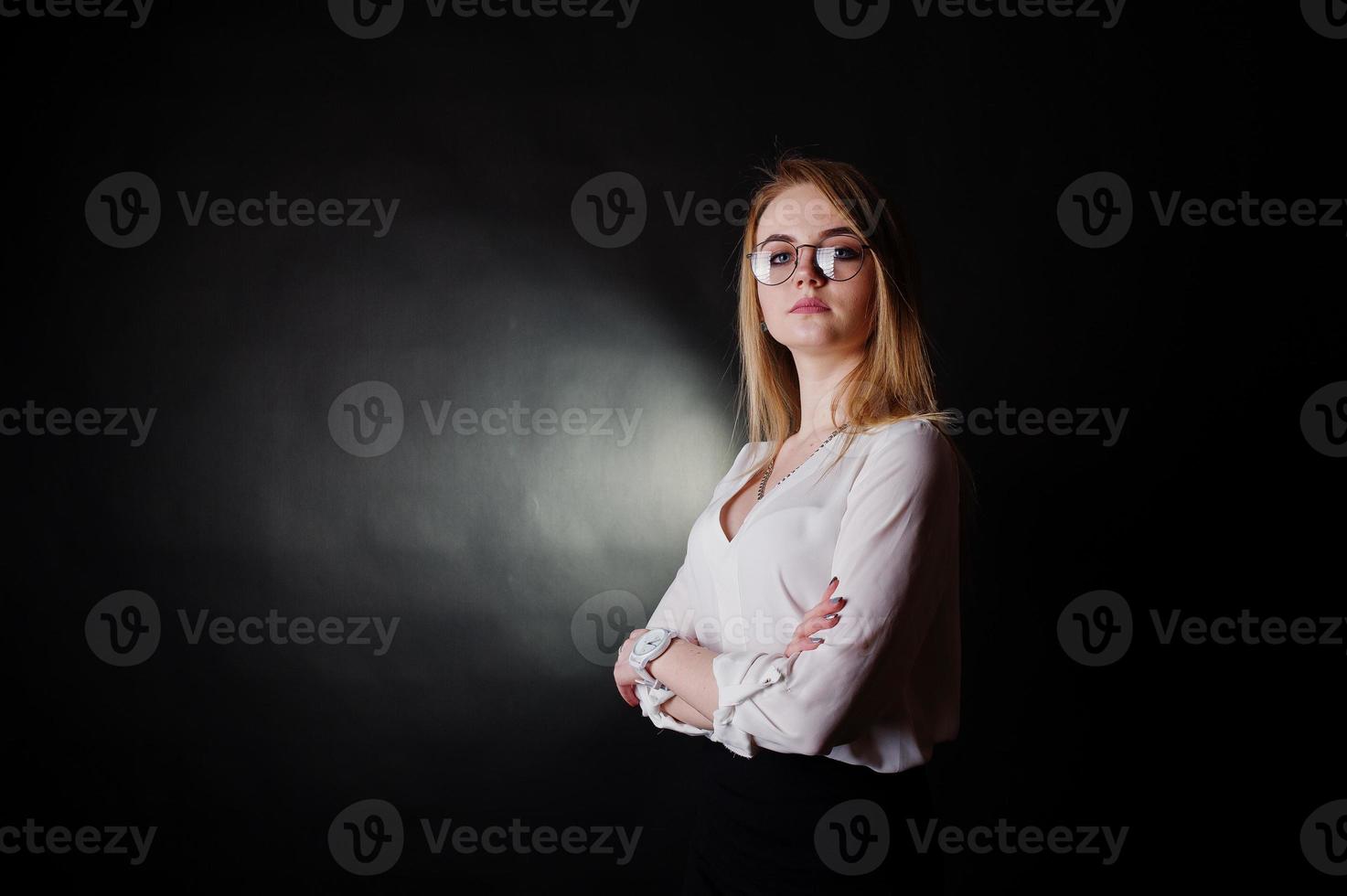 portrait en studio d'une femme d'affaires blonde à lunettes, chemisier blanc et jupe noire sur fond sombre. femme réussie et concept de fille élégante. photo