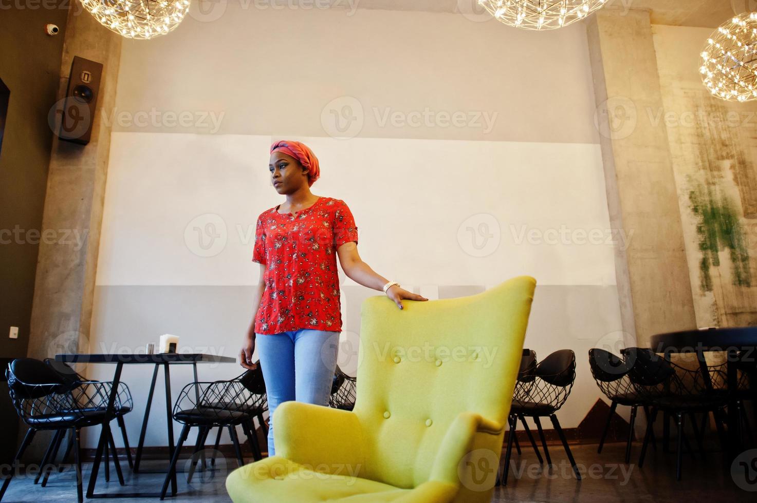 femme africaine élégante en chemise rouge et chapeau posé café intérieur. photo