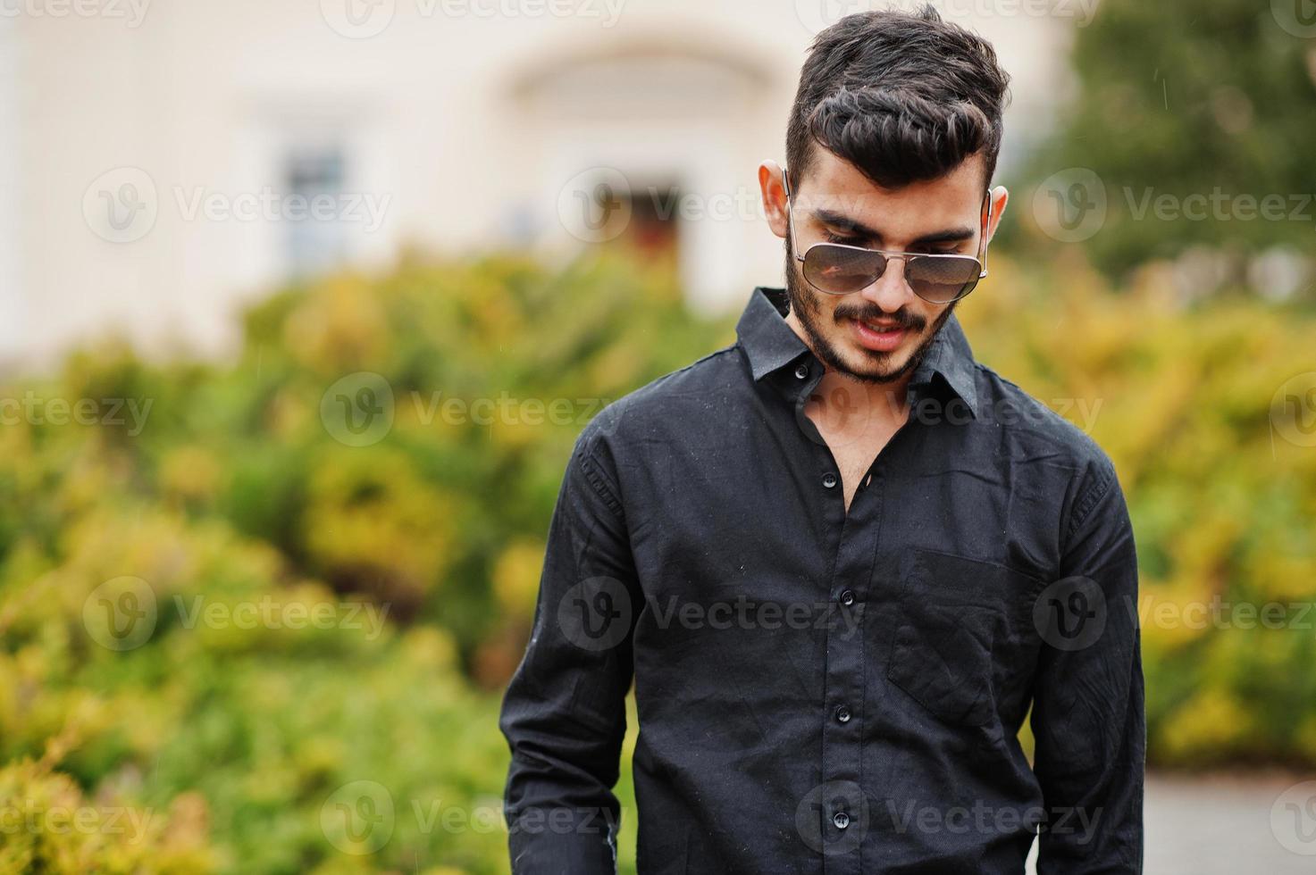 homme élégant indien en chemise noire et lunettes de soleil posées en plein air. photo