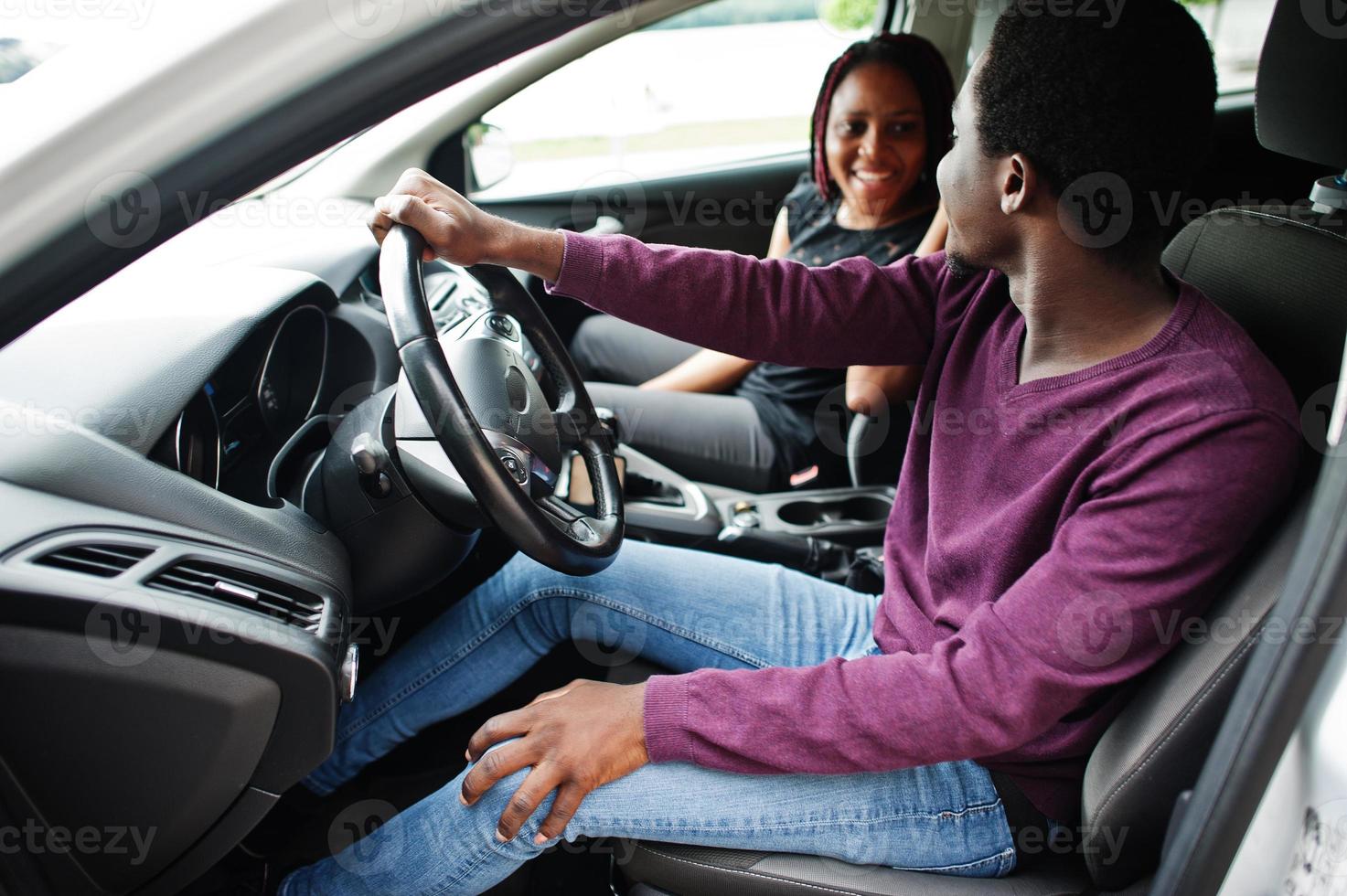 beau jeune couple afro-américain assis sur les sièges passagers avant tandis que bel homme conduisant une voiture. photo