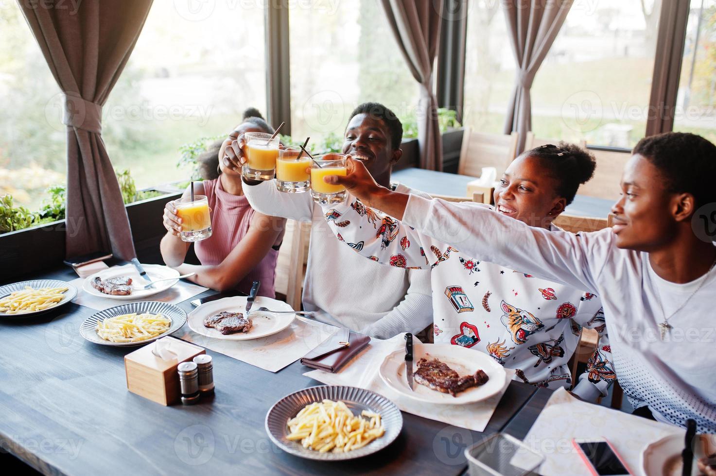 amis africains heureux assis, bavardant au café et mangeant de la nourriture. groupe de peuples noirs se réunissant au restaurant et dînant, acclamations. photo