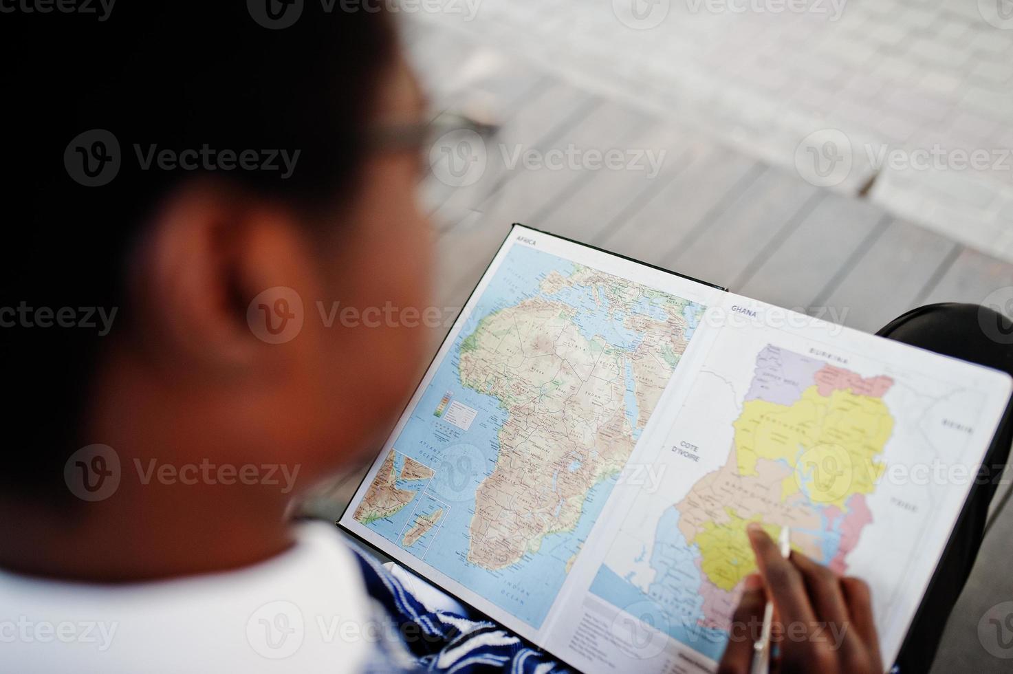 homme africain en vêtements traditionnels et lunettes regardant sur la carte de l'afrique et du ghana sur son carnet. photo