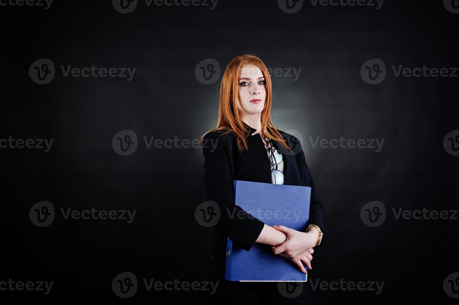 portrait d'une femme d'affaires rousse portant un chemisier rayé, des lunettes et une veste avec un dossier bleu. photo