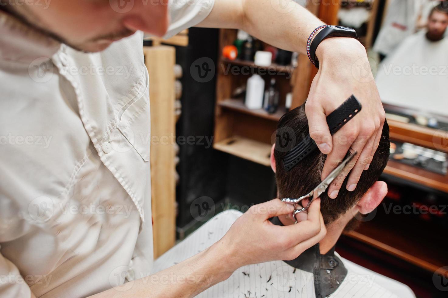 jeune homme barbu se coupe les cheveux par un coiffeur assis sur une chaise au salon de coiffure. âme de barbier. photo