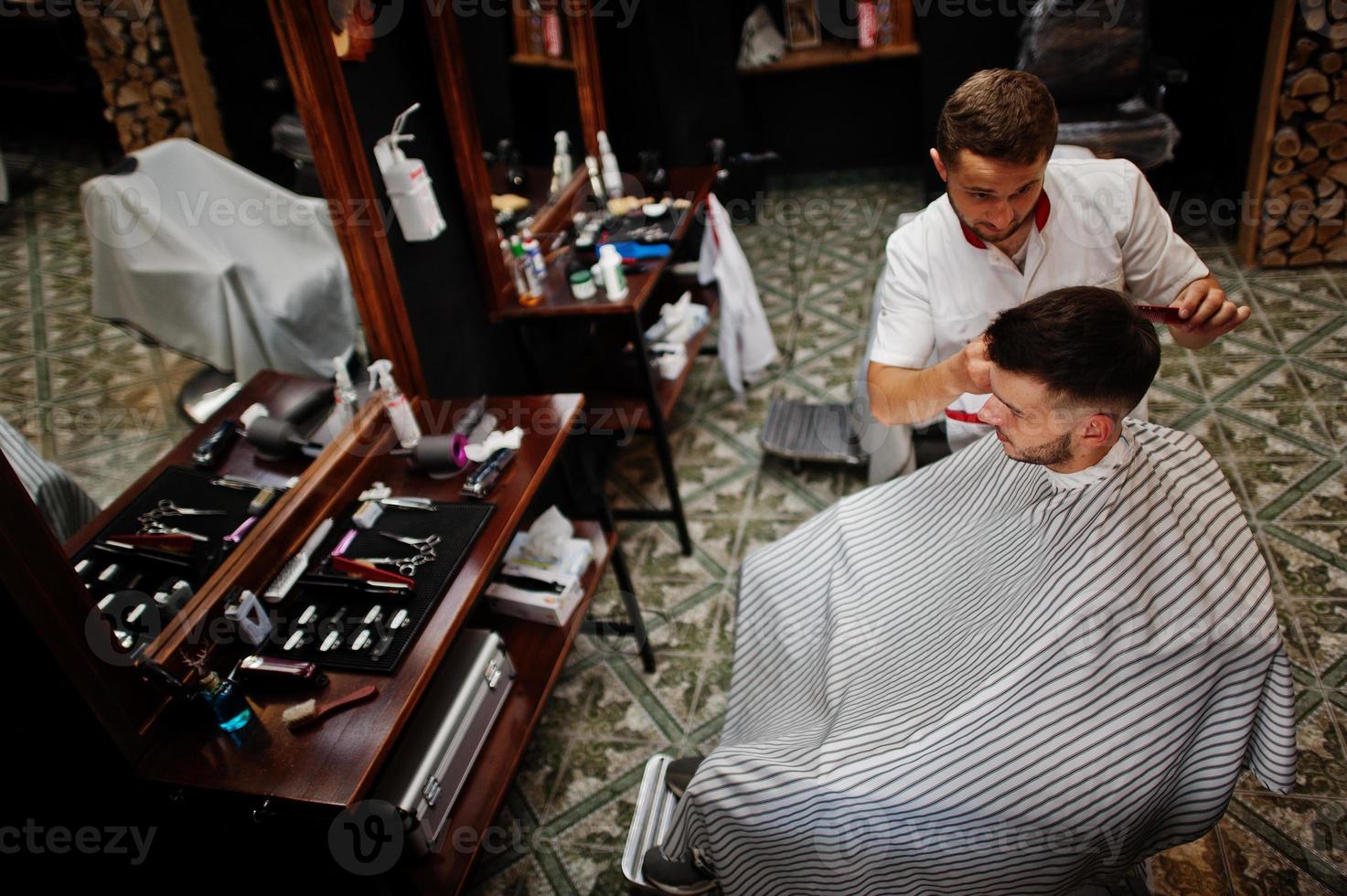 jeune homme barbu se coupe les cheveux par un coiffeur assis sur une chaise au salon de coiffure. âme de barbier. photo
