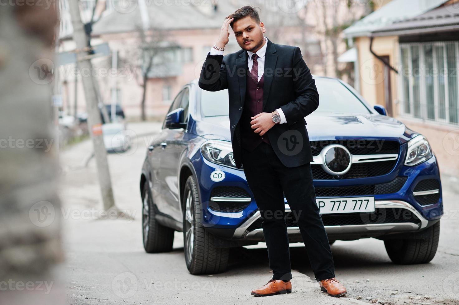 riche homme d'affaires indien en tenue de soirée debout contre une voiture suv d'affaires. photo