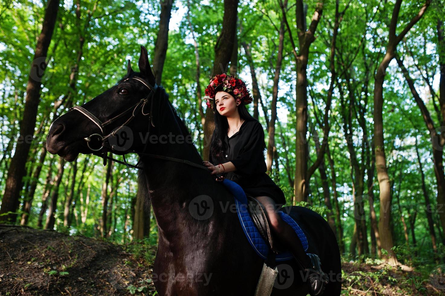 fille mystique en guirlande en noir à cheval en bois. photo