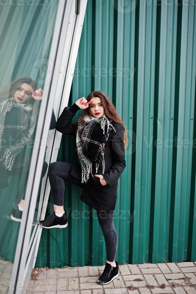 brune élégante fille décontractée en écharpe contre un mur métallique vert. photo