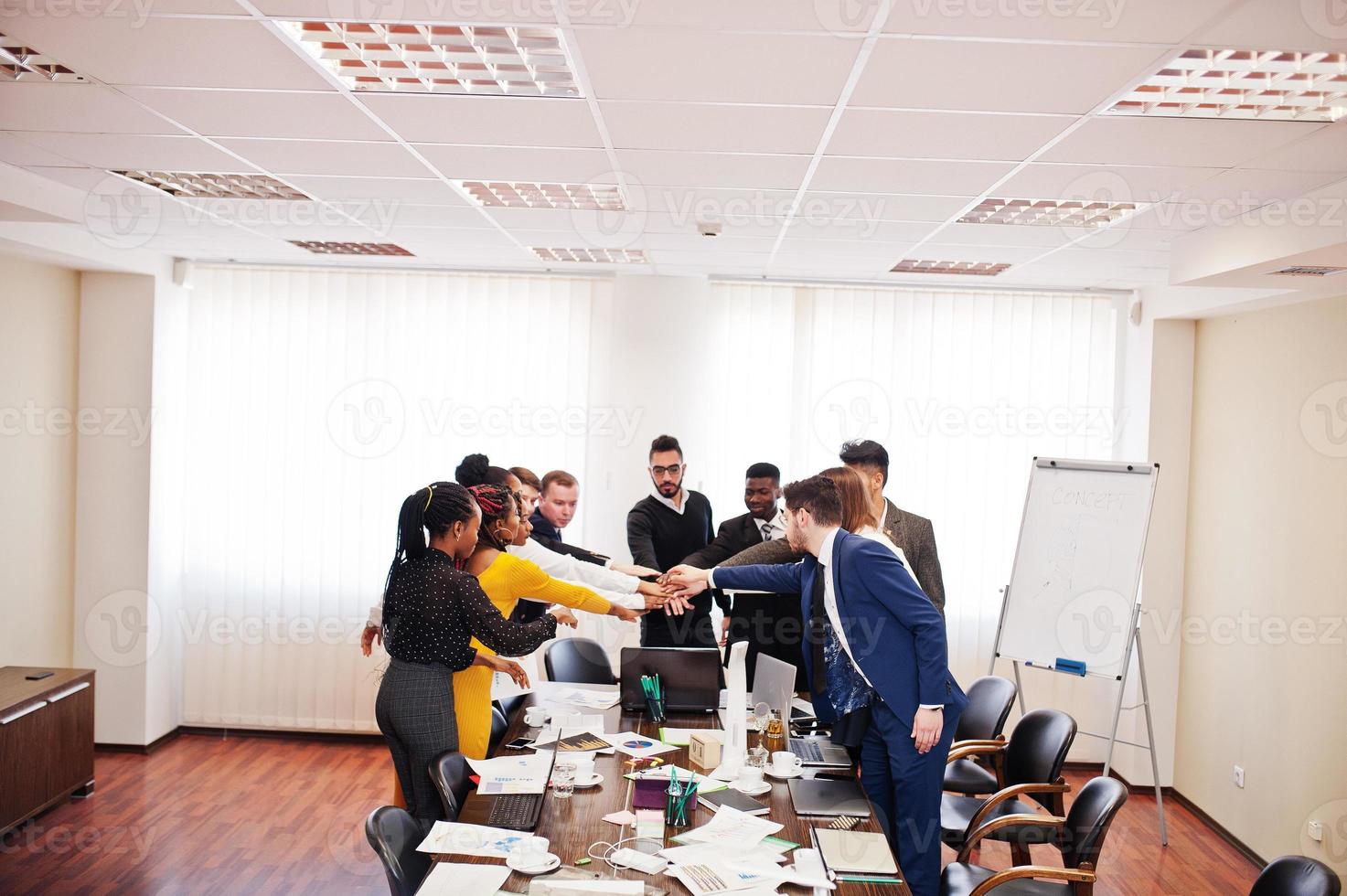 des hommes d'affaires multiraciaux debout au bureau et mettant la main sur la main. groupe diversifié d'employés en tenue de soirée. photo