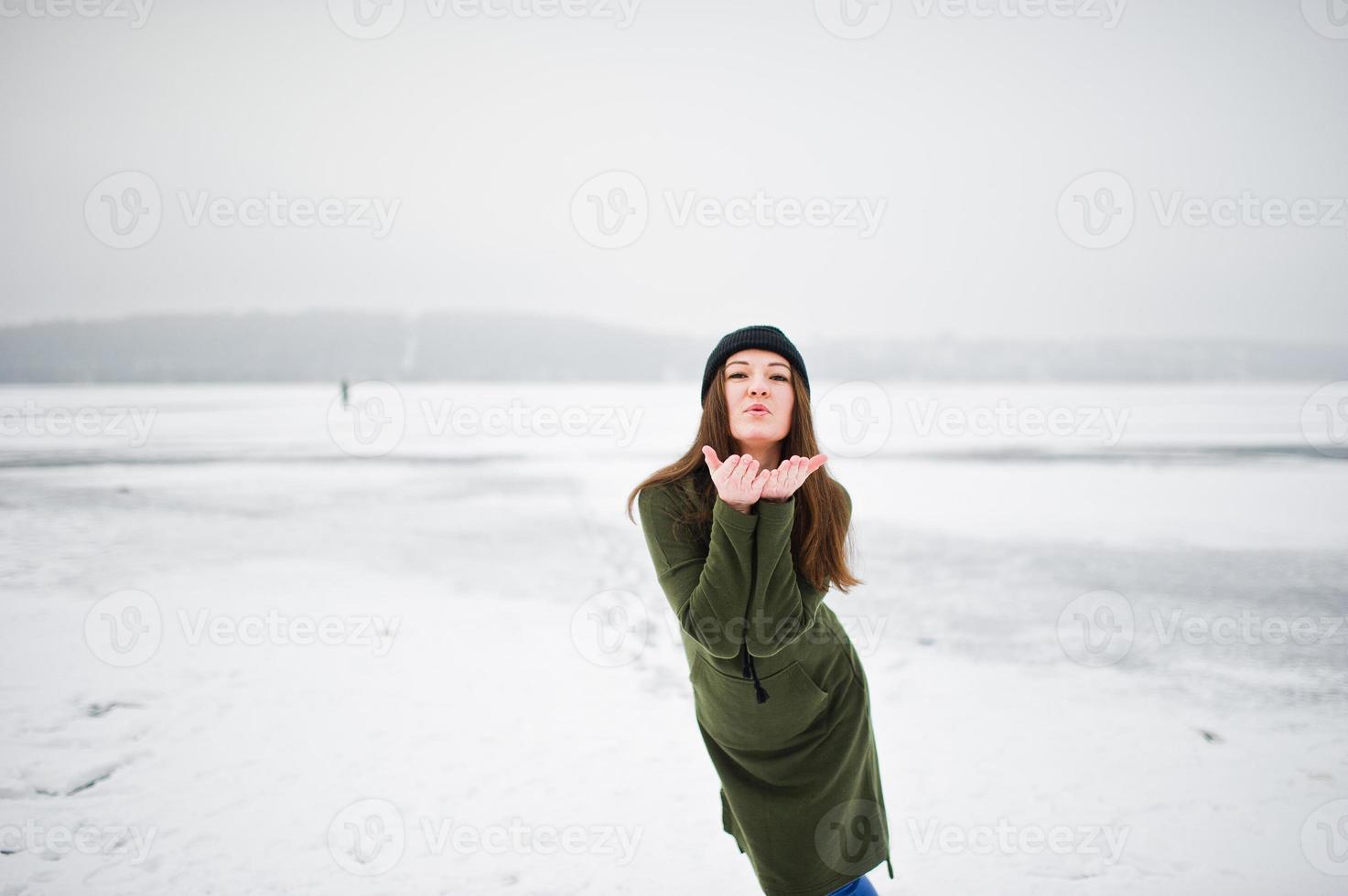 fille drôle portant un long sweat-shirt vert, un jean et un couvre-chef noir, au lac gelé en hiver. photo