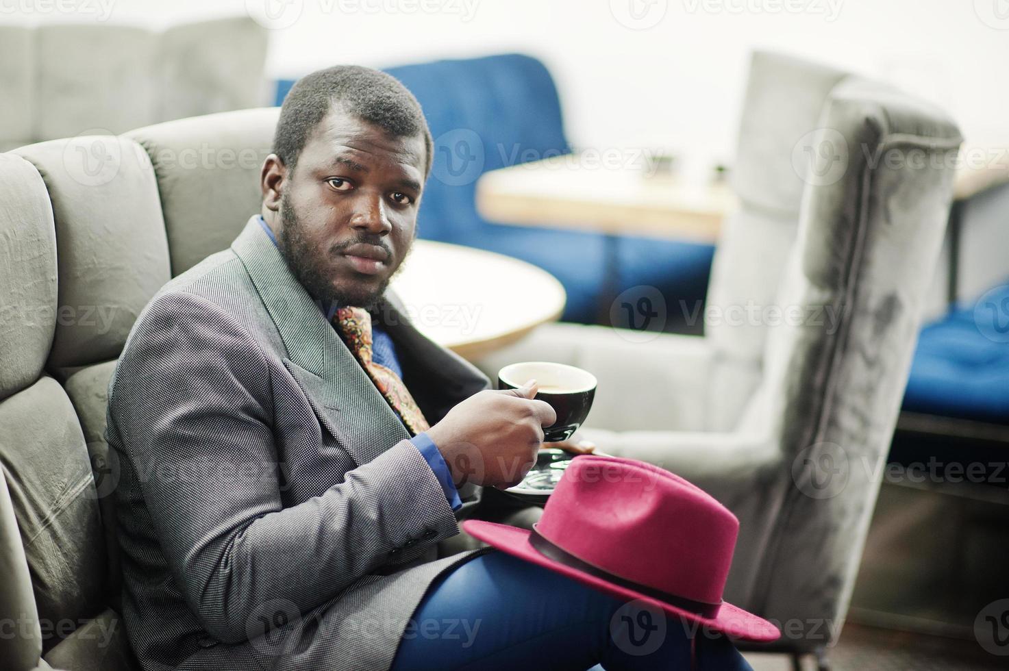 élégant modèle d'homme afro-américain en veste grise cravate et chapeau rouge boire du café au café. photo