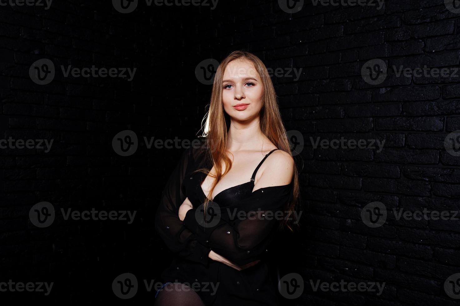 prise de vue en studio d'une jeune fille brune en chemisier noir avec soutien-gorge et short contre un mur de briques noires. photo