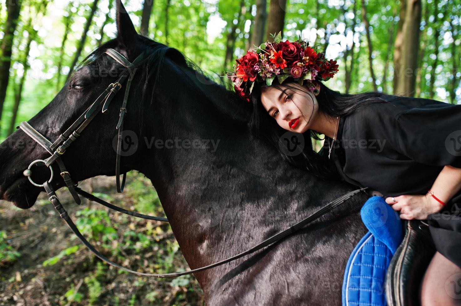 fille mystique en guirlande en noir à cheval en bois. photo