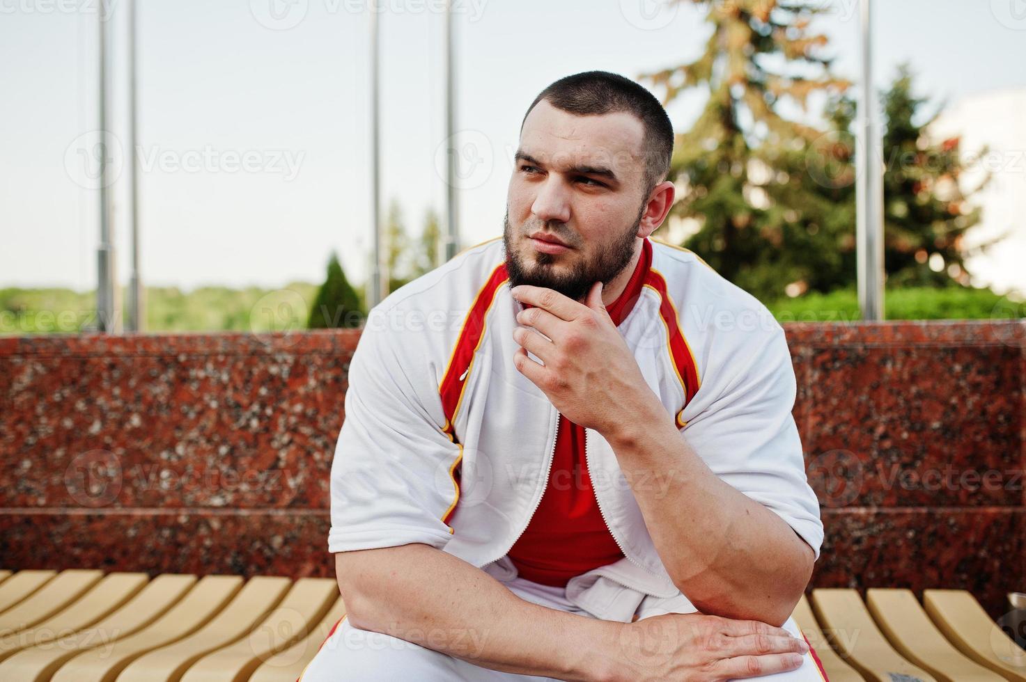 jeune homme musclé barbu brutal porte un costume de sport blanc avec une chemise rouge. photo