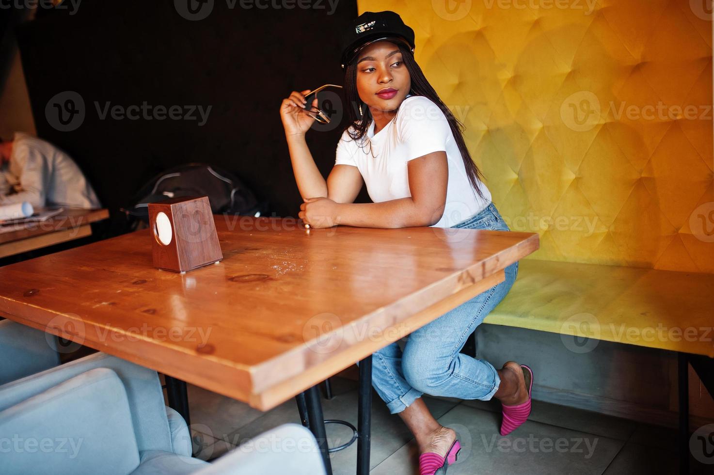 femme afro-américaine à la mode en casquette noire se relaxant dans un café confortable. photo