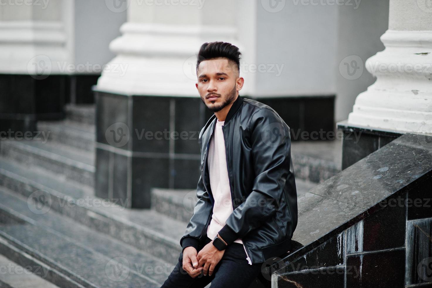 homme barbe indien élégant à la veste en cuir noir. modèle indien posé assis dans les rues de la ville. photo