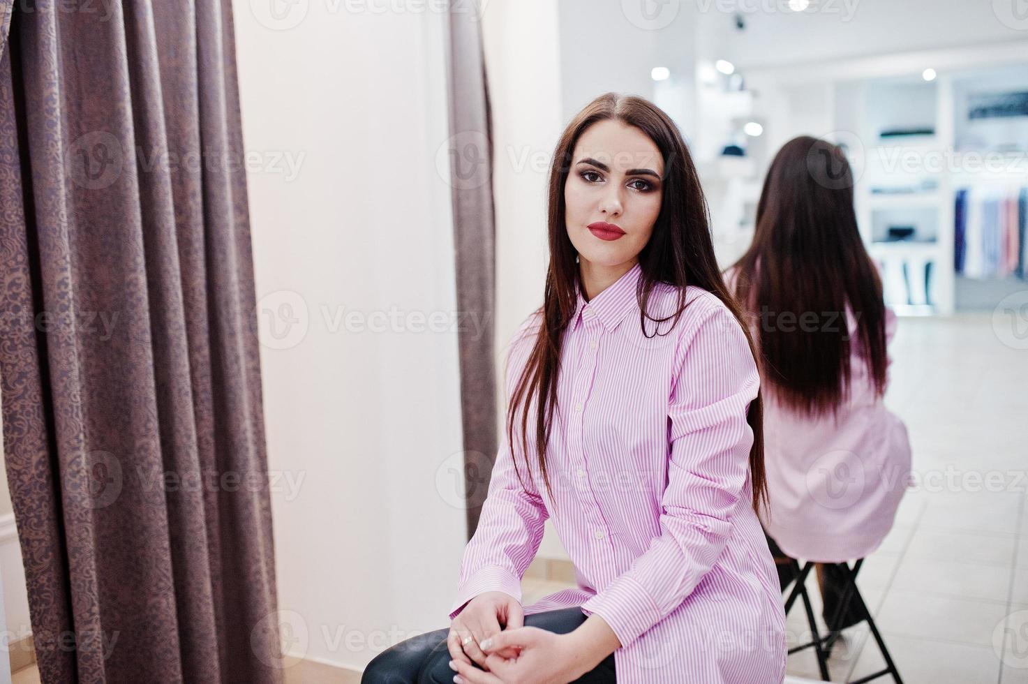 fille magnifique brune dans la boutique de vêtements décontractés et chemisier rose contre le miroir. photo