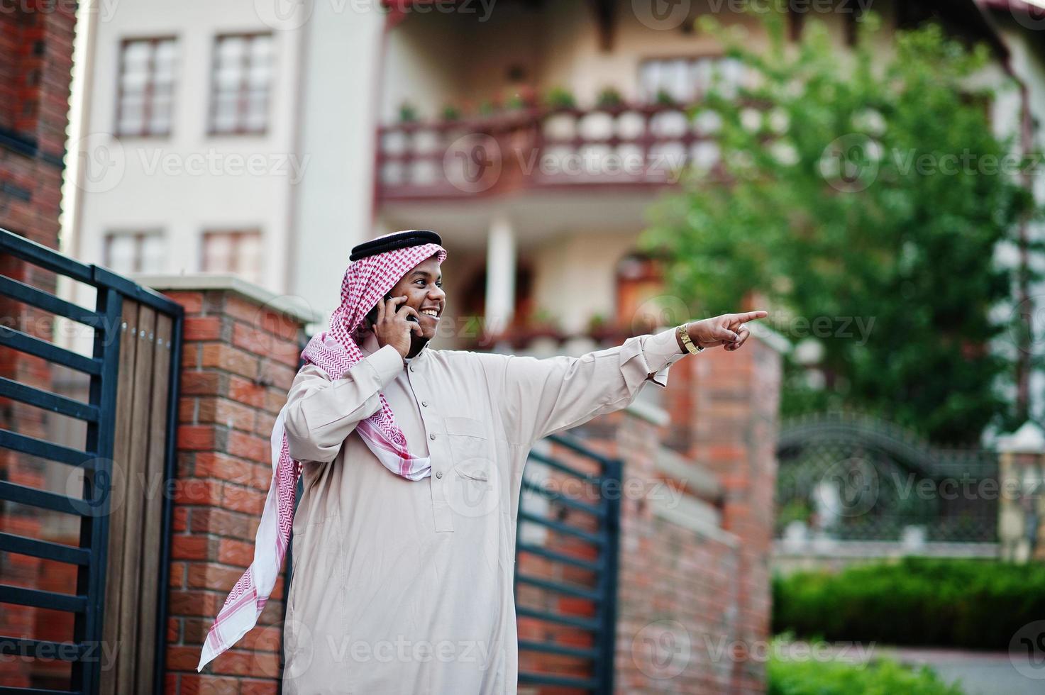 homme d'affaires arabe du moyen-orient posé dans la rue contre un bâtiment moderne avec téléphone portable et montrant le doigt. photo