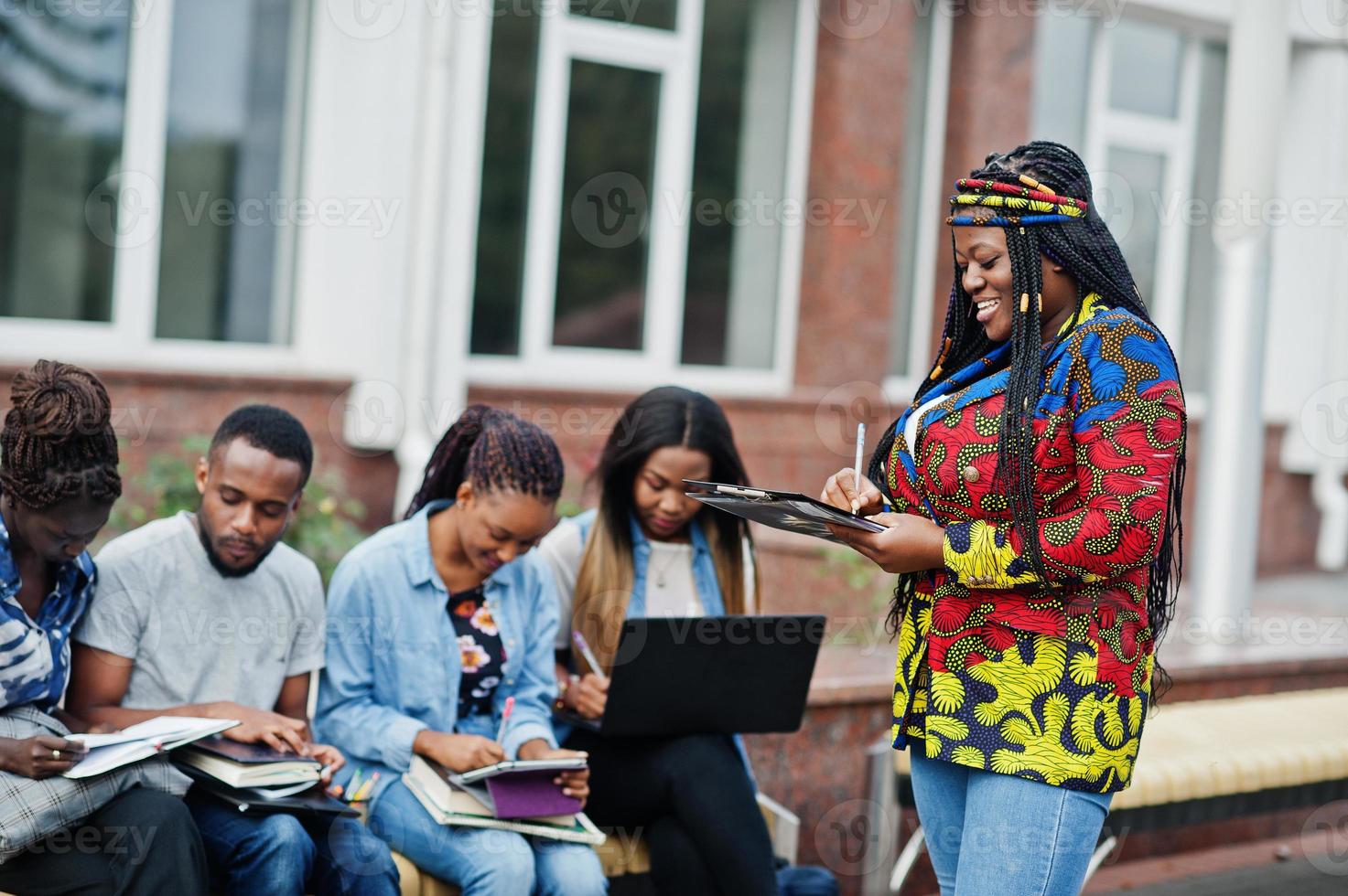 groupe de cinq étudiants africains qui passent du temps ensemble sur le campus de la cour universitaire. amis afro noirs étudiant au banc avec des articles scolaires, des cahiers d'ordinateurs portables. photo