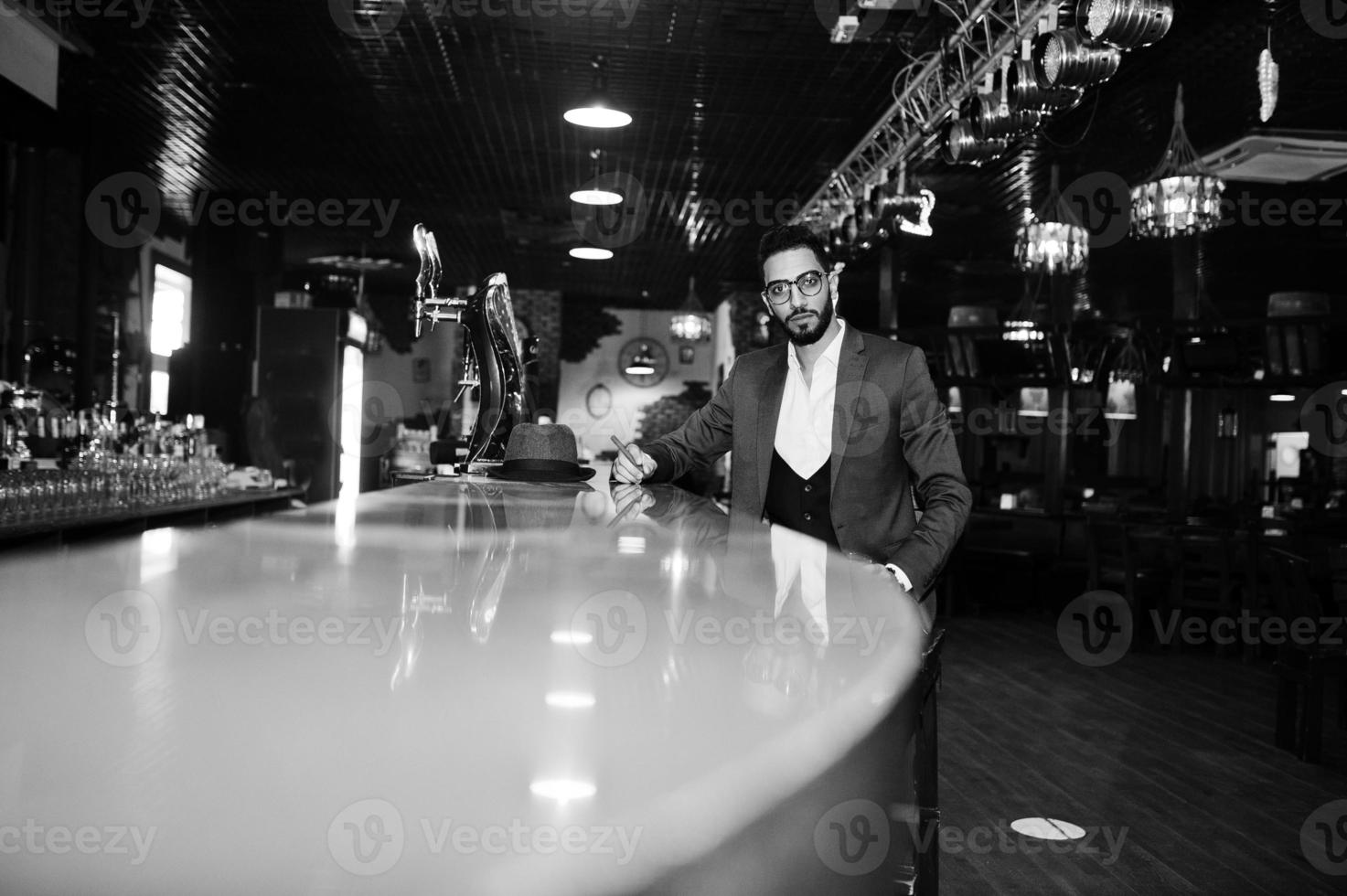 bel homme arabe bien habillé avec un verre de whisky et de cigare posé au pub. photo