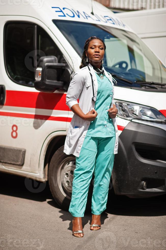 paramédic femme afro-américaine debout devant la voiture d'ambulance. photo