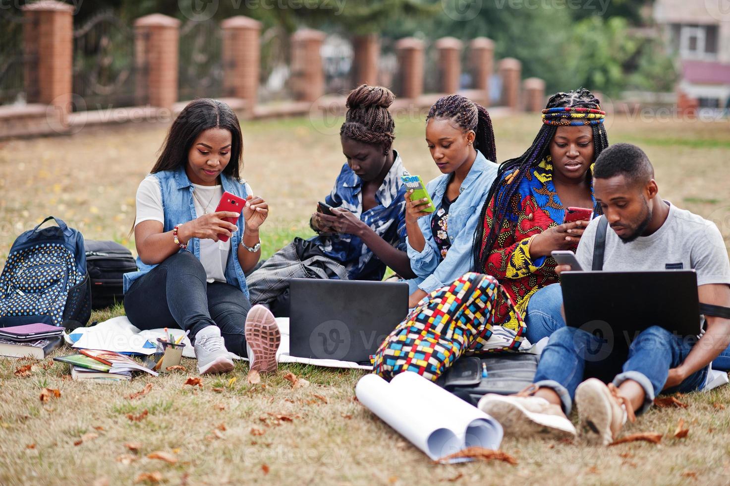 groupe de cinq étudiants africains qui passent du temps ensemble sur le campus de la cour universitaire. amis afro noirs faisant avec des téléphones portables. thème de l'éducation. photo