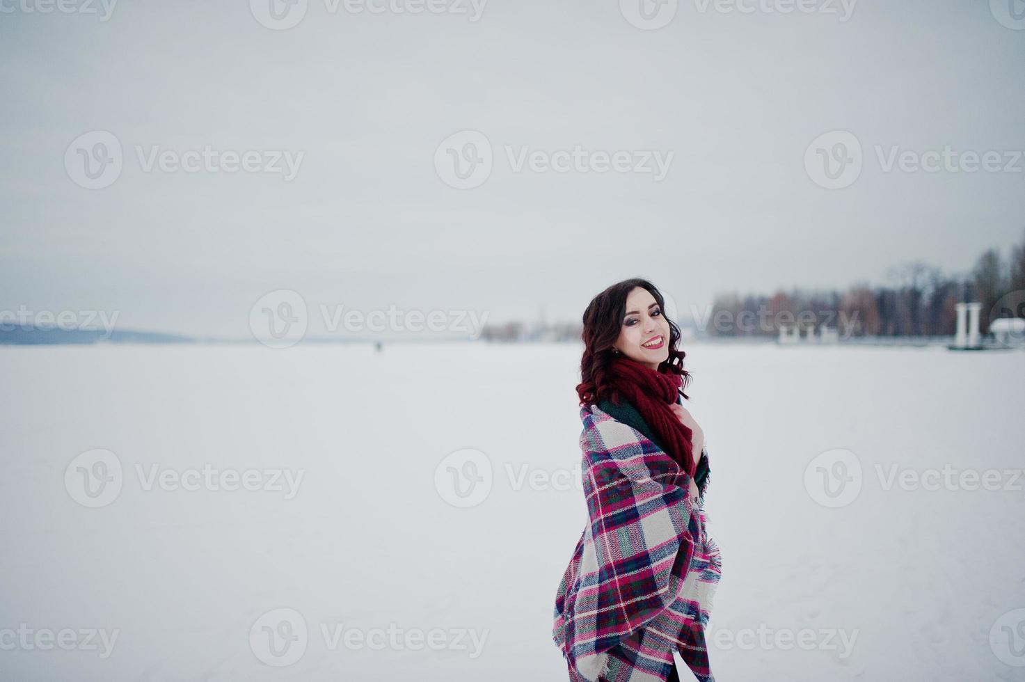 fille brune en pull vert et écharpe rouge avec lac gelé en plein air à carreaux le soir de la journée d'hiver. photo