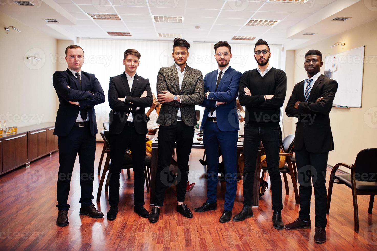 six hommes d'affaires multiraciaux debout au bureau avec les bras croisés. groupe diversifié d'employés masculins en tenue de soirée. photo