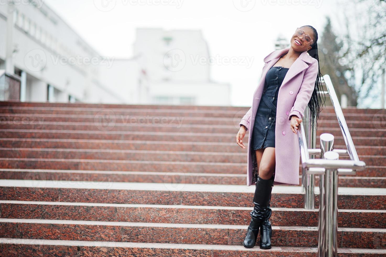 jeune élégante belle femme afro-américaine dans la rue contre les escaliers, portant un manteau de tenue de mode, des lunettes. photo