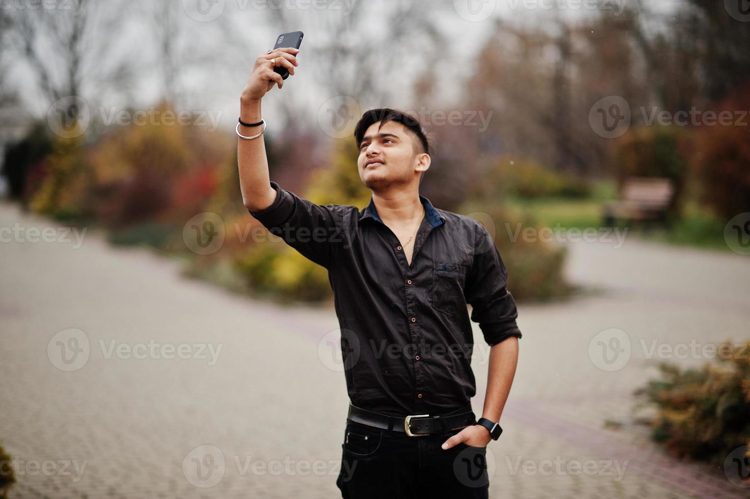 homme indien en chemise marron posé en plein air et faisant selfie sur téléphone mobile. photo