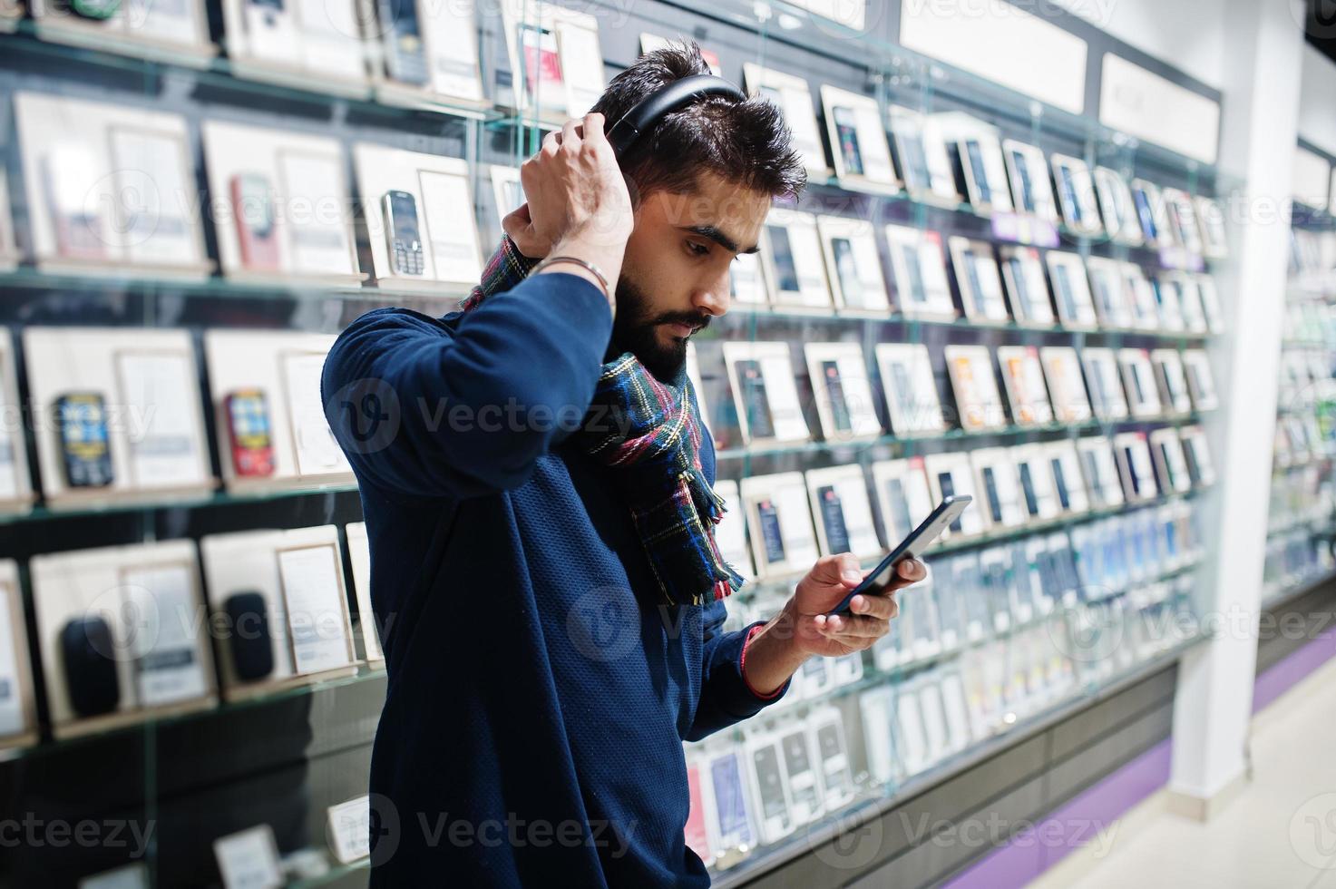 Acheteur client homme barbe indien au magasin de téléphonie mobile écouter de la musique à partir d'écouteurs sans fil se connecter à son smartphone. concept de peuples et de technologies d'asie du sud. magasin de téléphonie mobile. photo