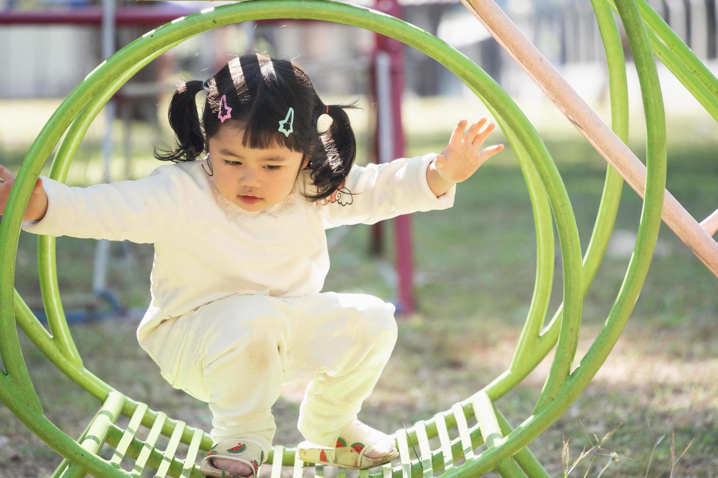 jolie fille asiatique joue dans la cour ou l'aire de jeux de l'école ou de la maternelle. activité estivale saine pour les enfants. petite fille asiatique grimpant à l'extérieur sur l'aire de jeux. enfant jouant sur une aire de jeux extérieure. photo