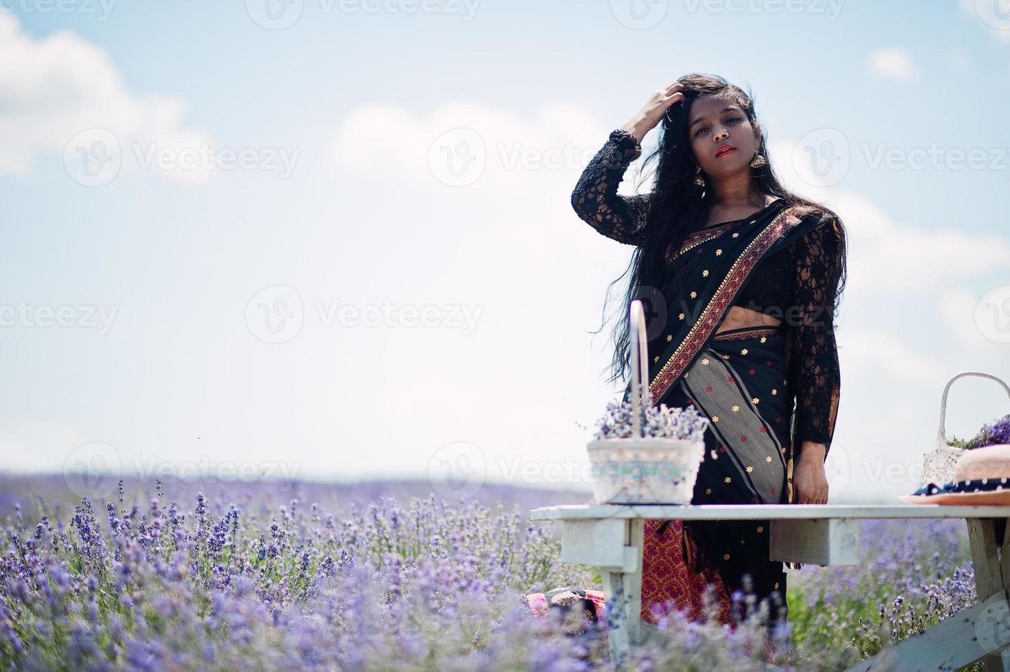 belle fille indienne porte une robe traditionnelle indienne saree dans un champ de lavande violette. photo