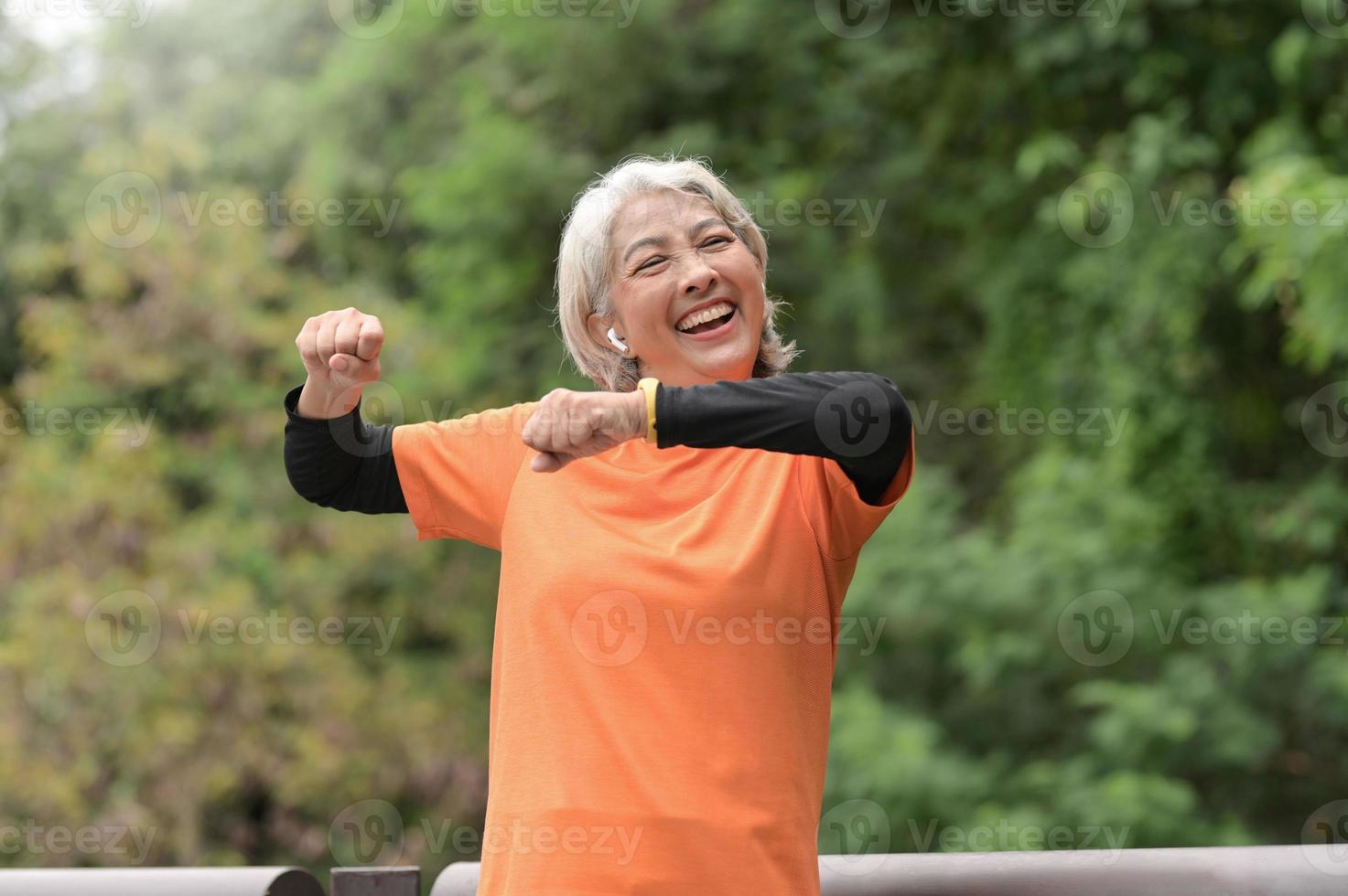 une femme asiatique à la retraite portant un t-shirt orange fait de l'exercice à l'extérieur, court, soulève des haltères, s'étire. photo