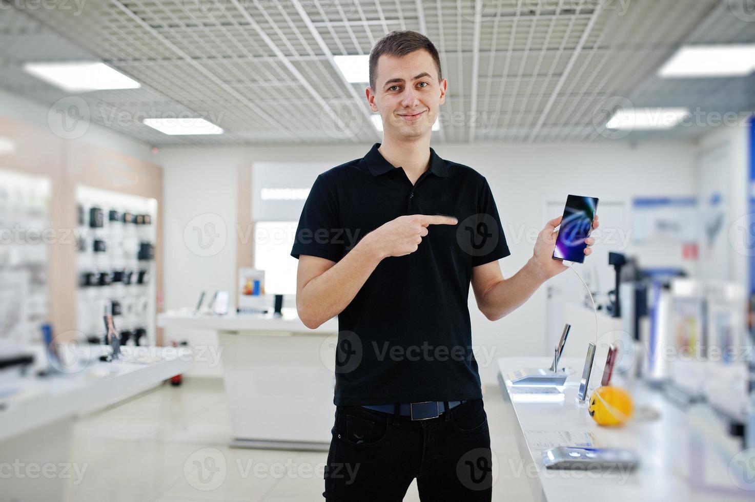 vendeur homme consultant professionnel en téléphonie mobile dans un magasin de technologie ou un magasin tenir un nouveau smartphone à portée de main et montrer le doigt à l'écran. photo