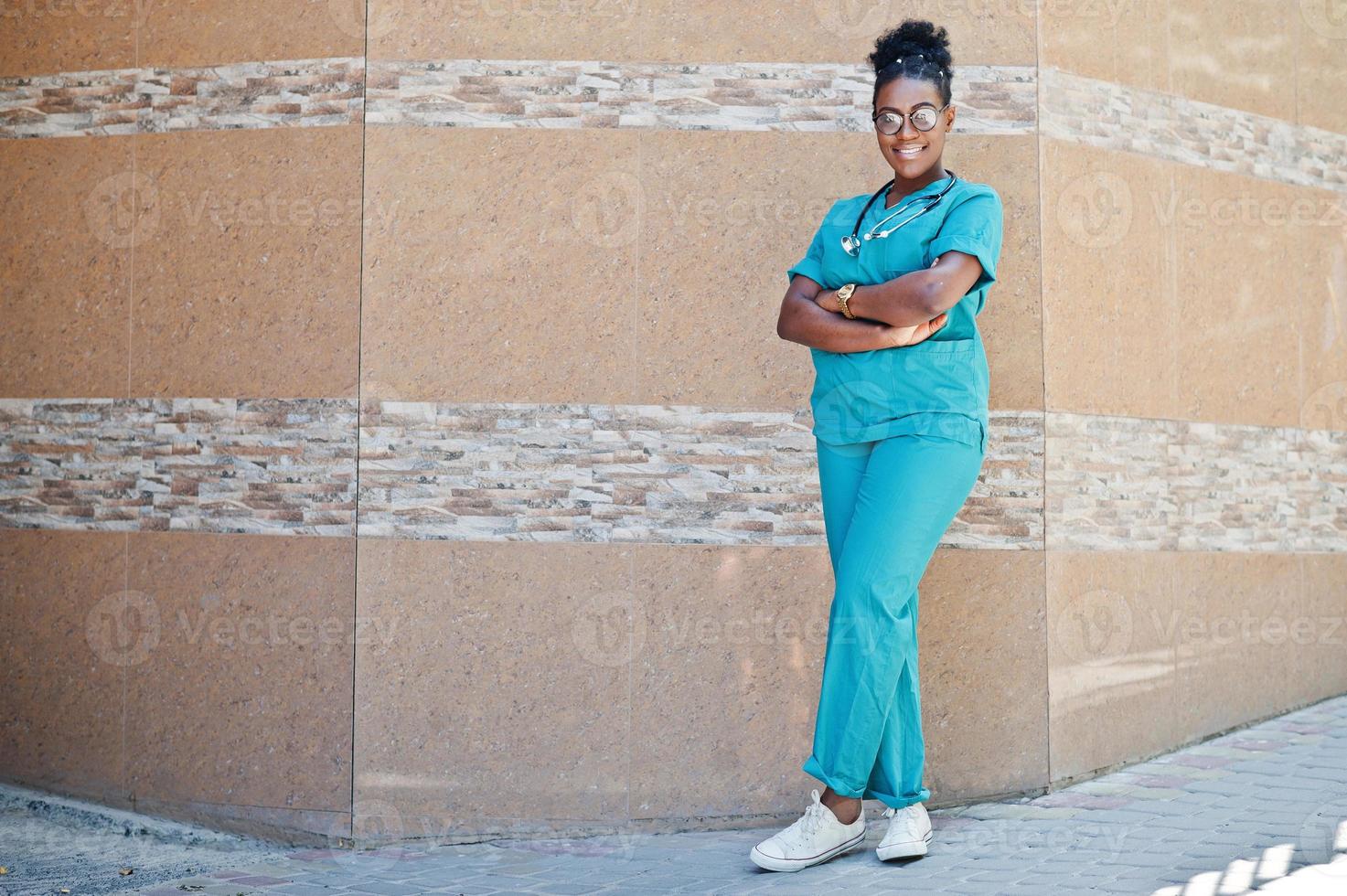 femme médecin afro-américaine en blouse de laboratoire avec stéthoscope posé en plein air contre la clinique. photo