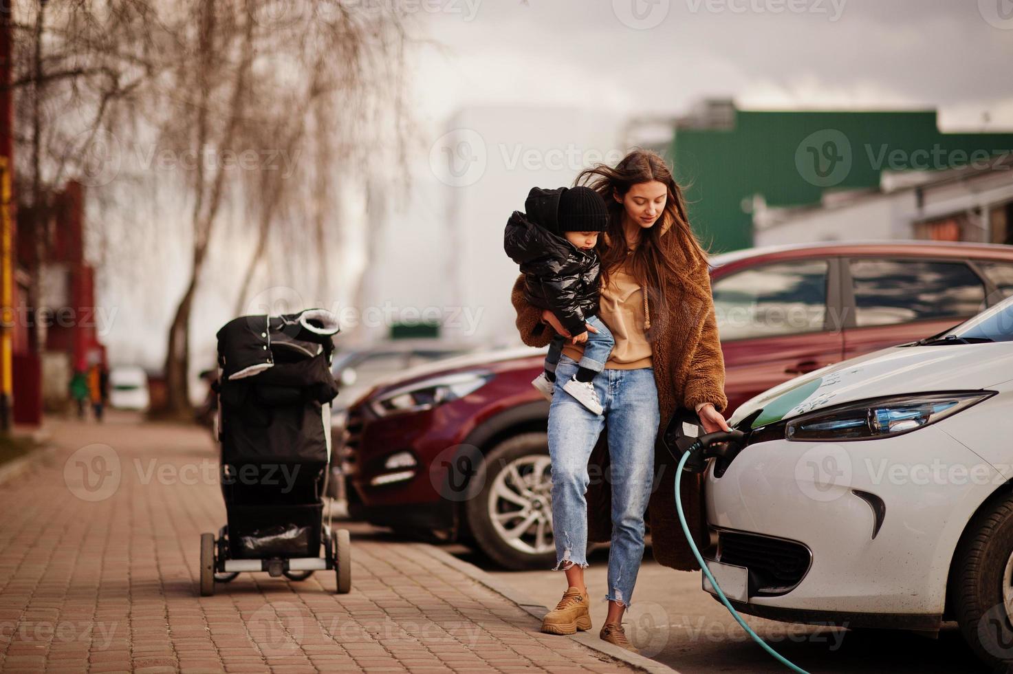 jeune mère avec enfant chargeant une voiture électrique à la station-service électrique. photo