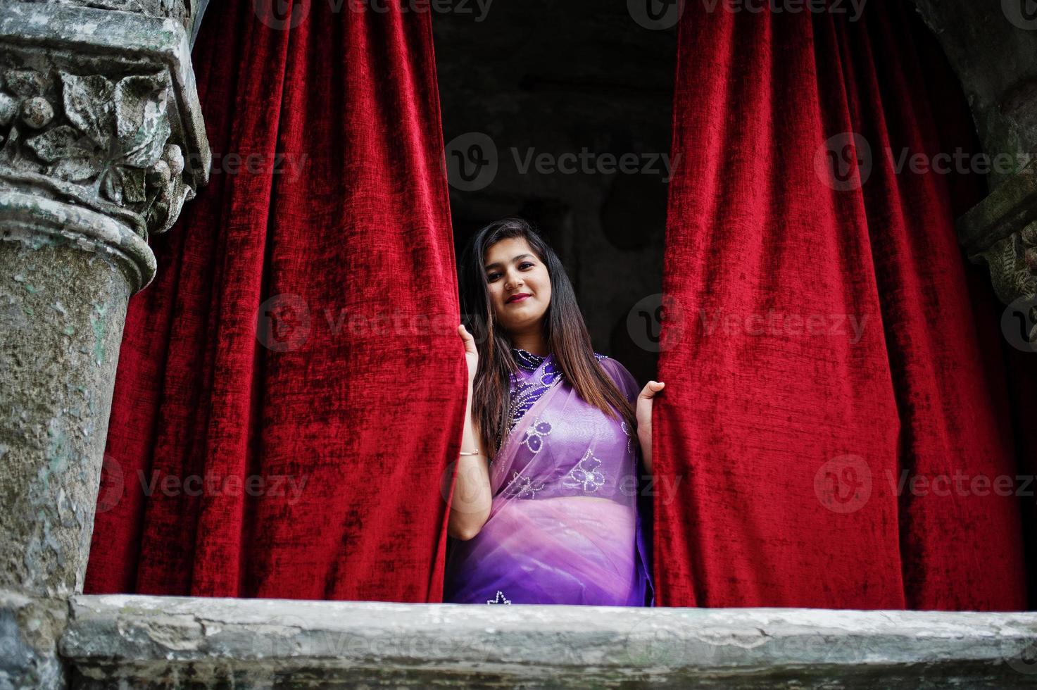 fille hindoue indienne au sari violet traditionnel posé dans la rue contre la vieille maison avec des rideaux rouges. photo