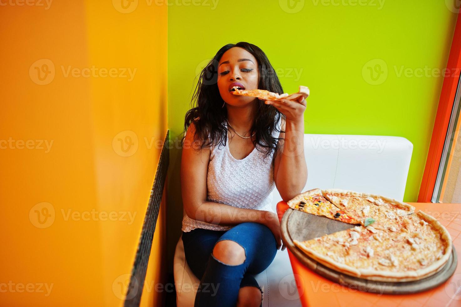 femme africaine avec pizza assis au restaurant aux couleurs vives. photo