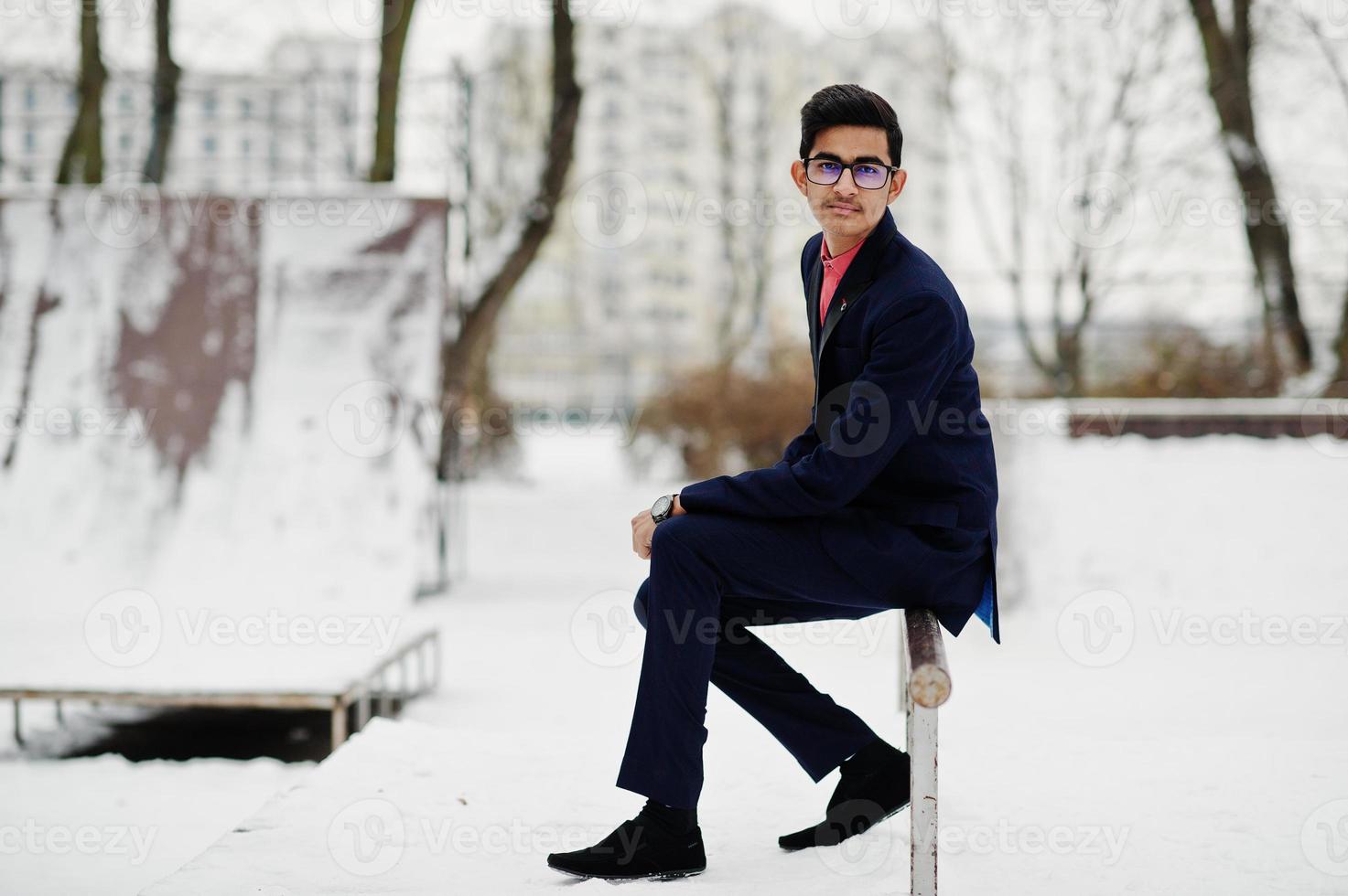 homme étudiant indien élégant en costume et lunettes posé à la journée d'hiver en plein air. photo