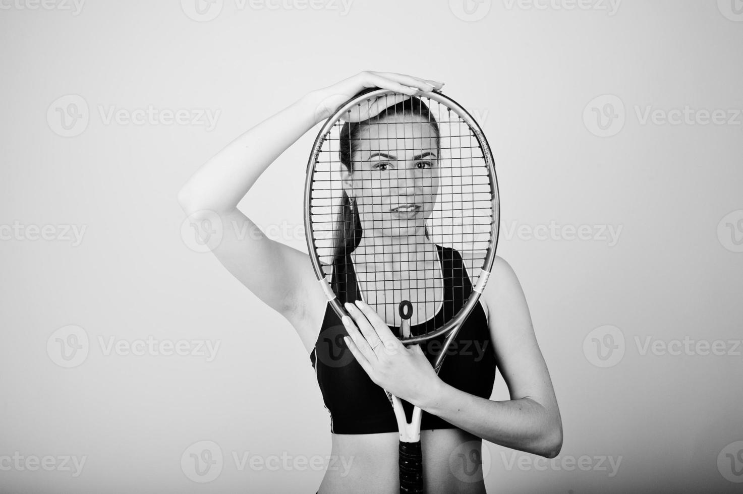 portrait noir et blanc de la belle jeune femme joueuse en vêtements de sport tenant une raquette de tennis en se tenant debout sur fond blanc. photo