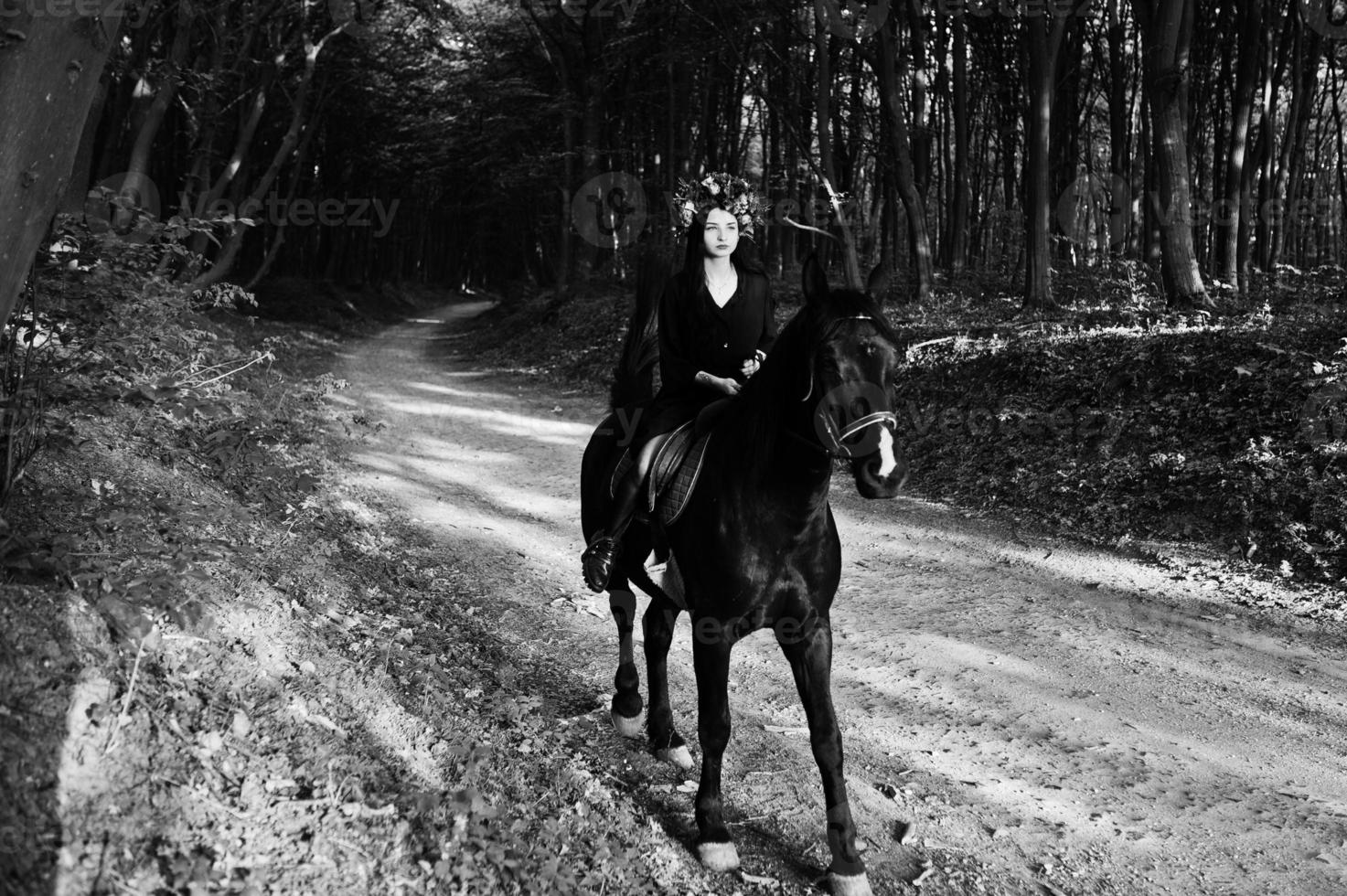 fille mystique en guirlande en noir à cheval en bois. photo