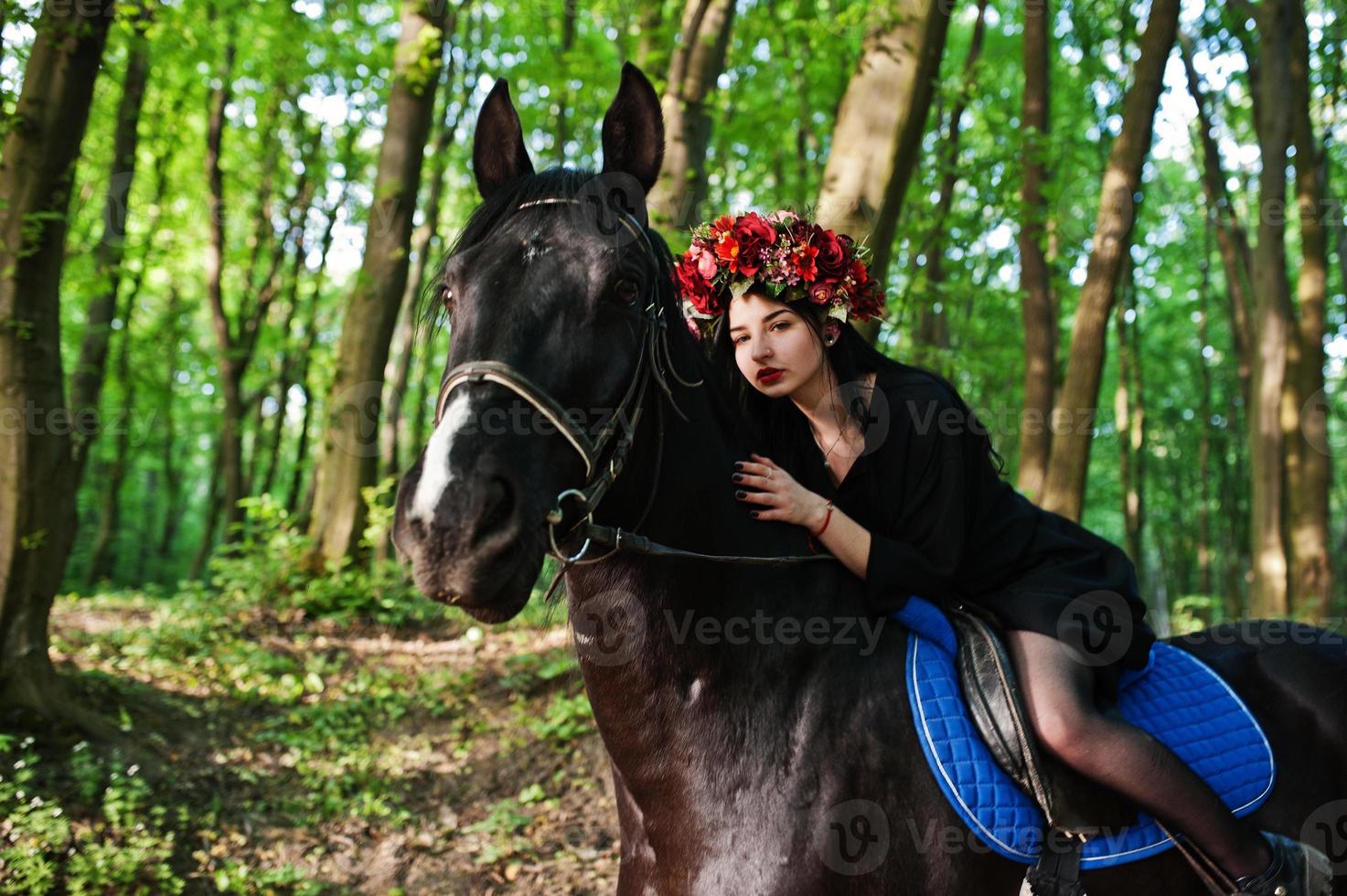 fille mystique en guirlande en noir à cheval en bois. photo