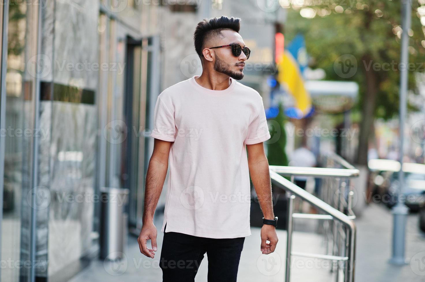 homme barbe indien élégant à lunettes de soleil et t-shirt rose. modèle indien posé en plein air dans les rues de la ville. photo