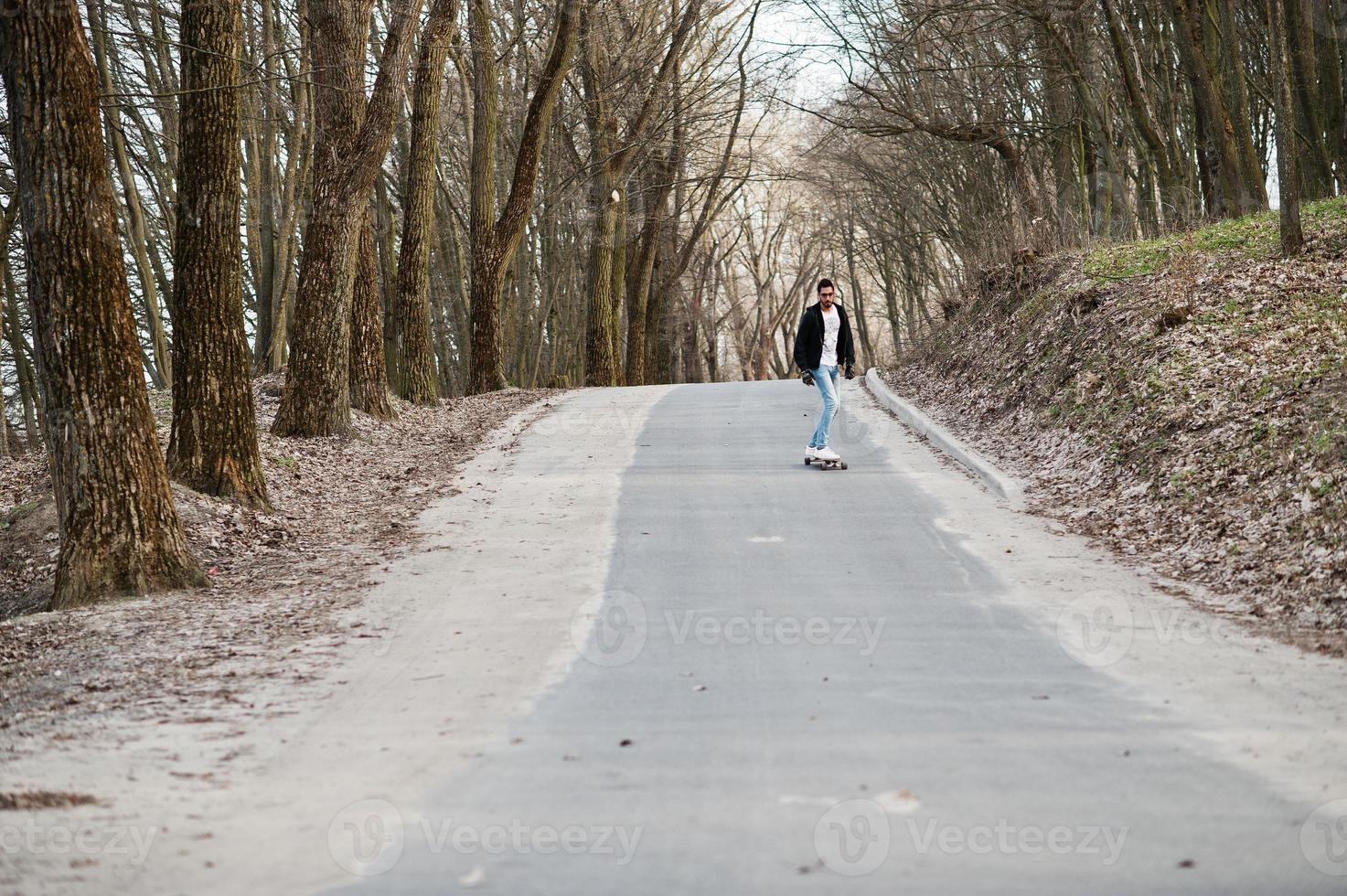 homme arabe de style de rue à lunettes avec longboard longboard sur la route. photo