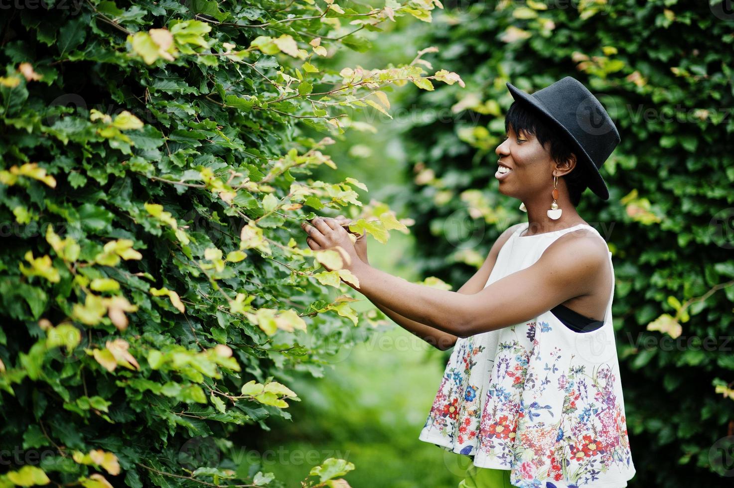 incroyable femme modèle afro-américaine en pantalon vert et chapeau noir posé au parc. photo