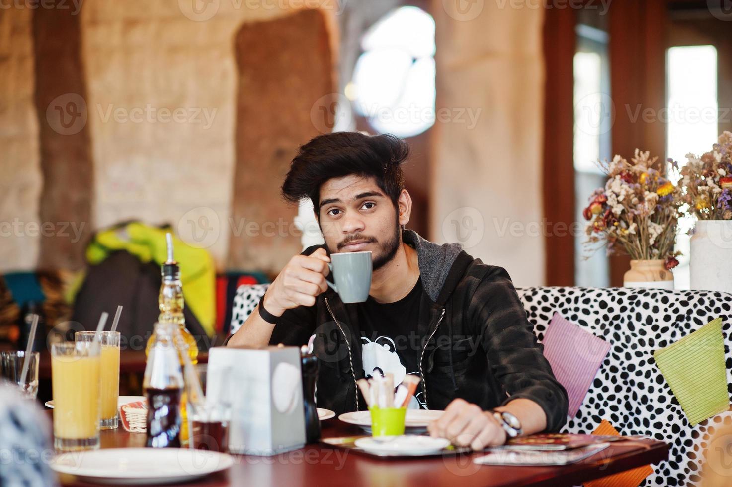 barbe homme asiatique en tenue décontractée assis café intérieur et boire du café. photo