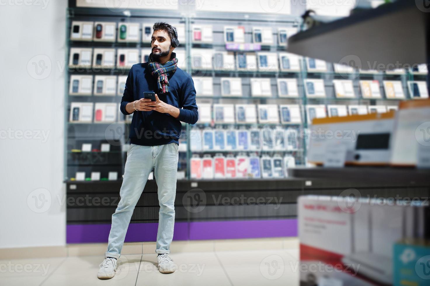 Acheteur client homme barbe indien au magasin de téléphonie mobile écouter de la musique à partir d'écouteurs sans fil se connecter à son smartphone. concept de peuples et de technologies d'asie du sud. magasin de téléphonie mobile. photo